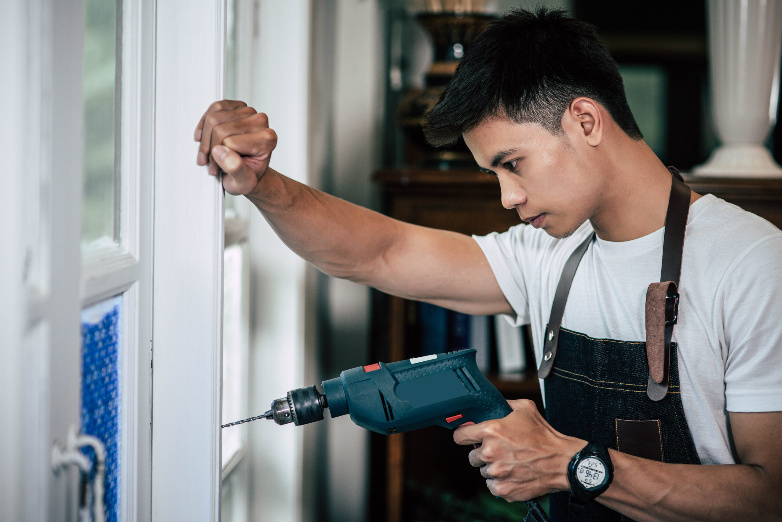 The carpenter holds the drill and drills the window. Selective focus.